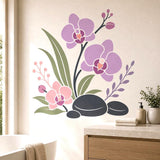 Three lavender and blush orchids with green leaves and dark branches above black stones, shown on a bathroom wall.