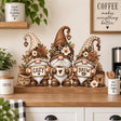 Three coffee gnomes with patterned hats, COZY and BREW signs, a heart mug, flowers and coffee beans above a kitchen coffee station.