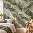 Green camouflage wall mural behind a bed with sage, olive, beige and cream shapes, topographic lines, grids and distressed details.