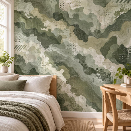 Green camouflage wall mural behind a bed with sage, olive, beige and cream shapes, topographic lines, grids and distressed details.
