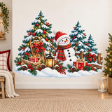 Snowman in a red hat and striped scarf beside a Christmas tree, snowy evergreens, gifts, a sled, lantern and rustic fence.